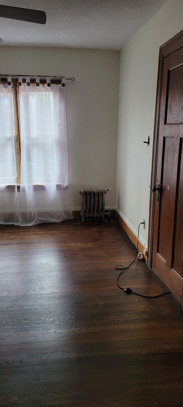 spare room featuring ceiling fan, radiator heating unit, dark wood-type flooring, and a textured ceiling