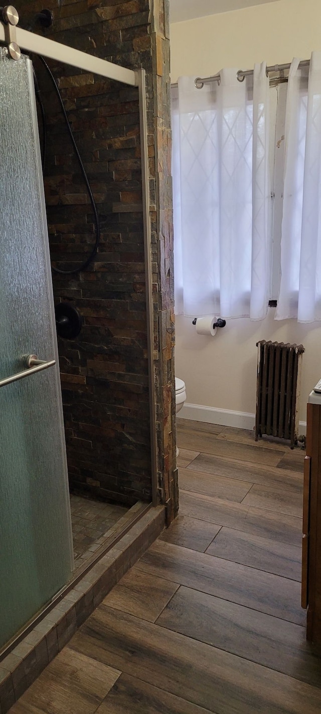 bathroom featuring toilet, radiator heating unit, a shower with door, and hardwood / wood-style flooring