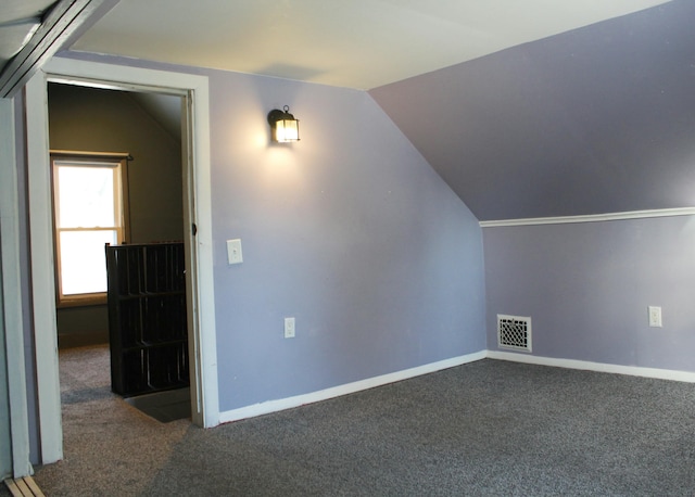 additional living space with dark colored carpet and vaulted ceiling