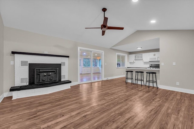 unfurnished living room with ceiling fan, a fireplace, vaulted ceiling, and light wood-type flooring