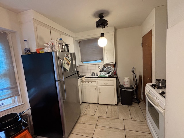 kitchen with stainless steel refrigerator, gas range gas stove, backsplash, white cabinets, and decorative light fixtures