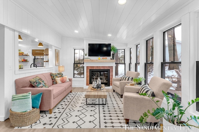 living room featuring wood ceiling, light wood-type flooring, and a brick fireplace