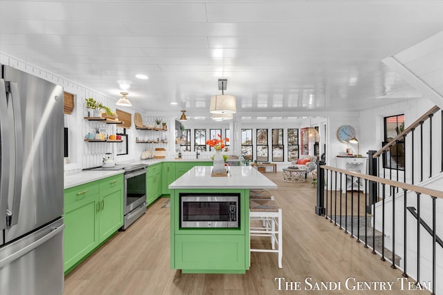 kitchen with stainless steel appliances, green cabinetry, decorative light fixtures, light wood-type flooring, and a kitchen island