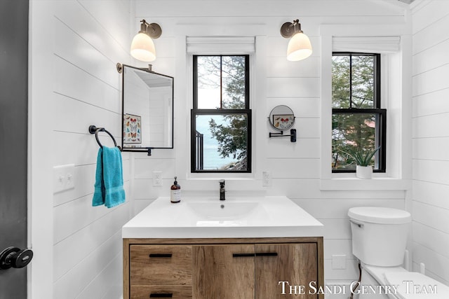 bathroom featuring toilet, vanity, wood walls, and a healthy amount of sunlight