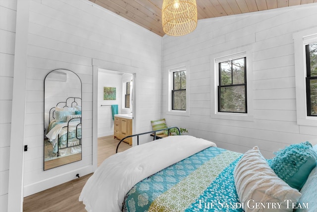 bedroom featuring connected bathroom, vaulted ceiling, multiple windows, and hardwood / wood-style flooring