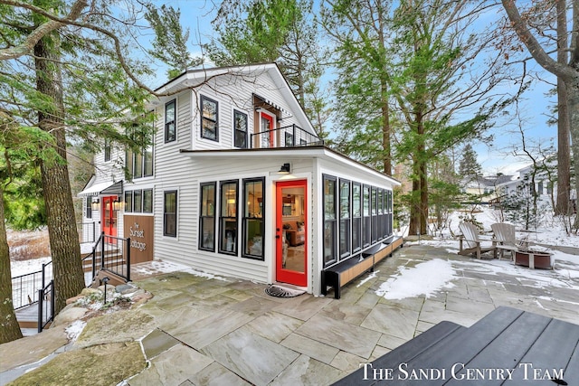 snow covered house featuring a sunroom and a patio