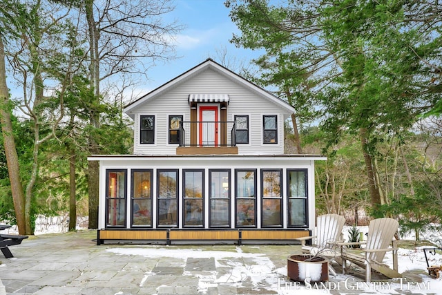 snow covered back of property featuring a patio and a sunroom