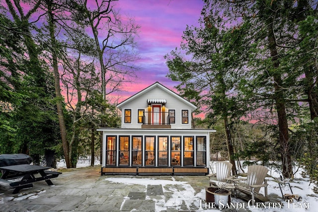 back house at dusk featuring a patio area and a sunroom