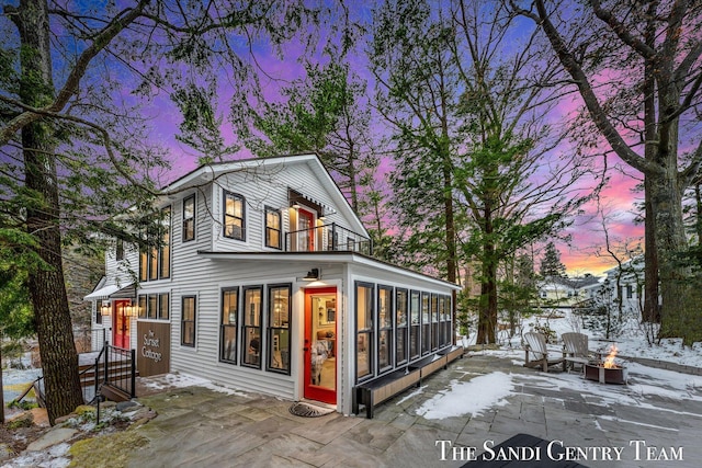 snow covered house with a sunroom, a patio area, and a fire pit