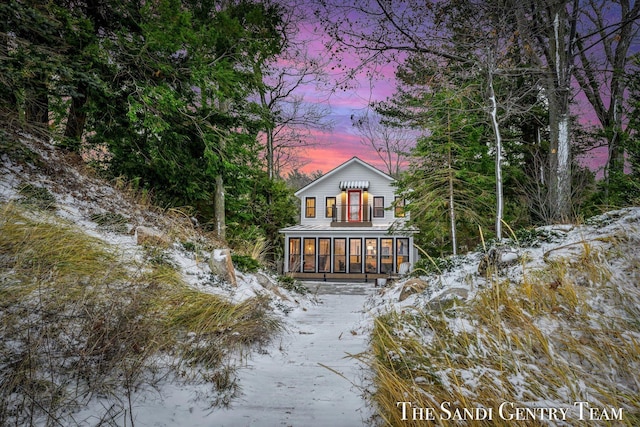 snow covered back of property featuring a sunroom