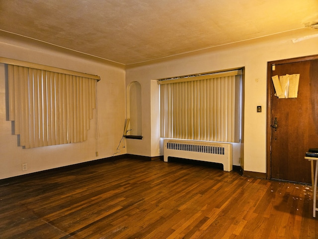 empty room with dark wood-type flooring and radiator