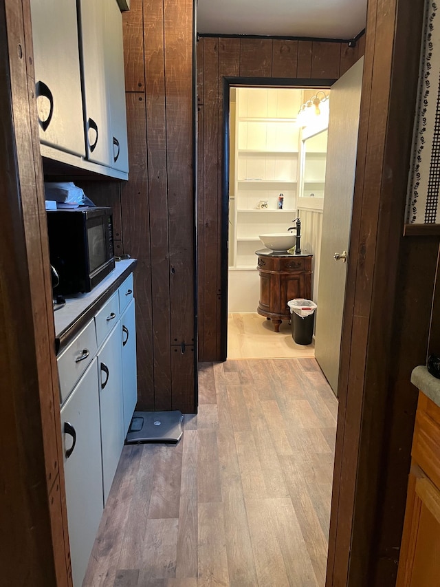 kitchen with wooden walls, white cabinets, and light wood-type flooring