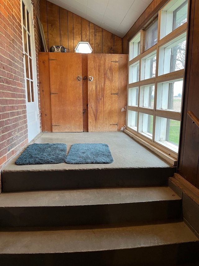 staircase with wood walls, lofted ceiling, and brick wall