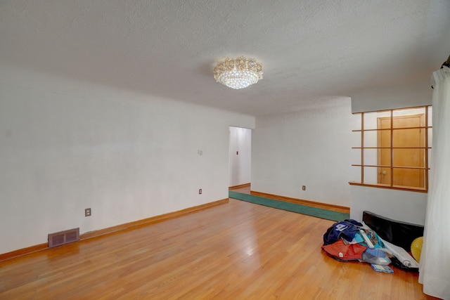 unfurnished room featuring wood-type flooring, a textured ceiling, and an inviting chandelier