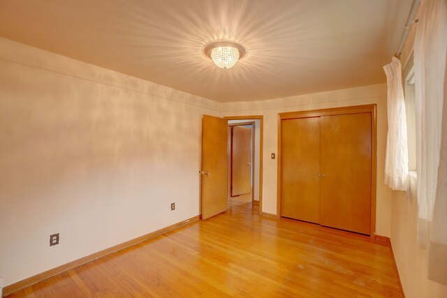 unfurnished bedroom featuring wood-type flooring, an inviting chandelier, and a closet