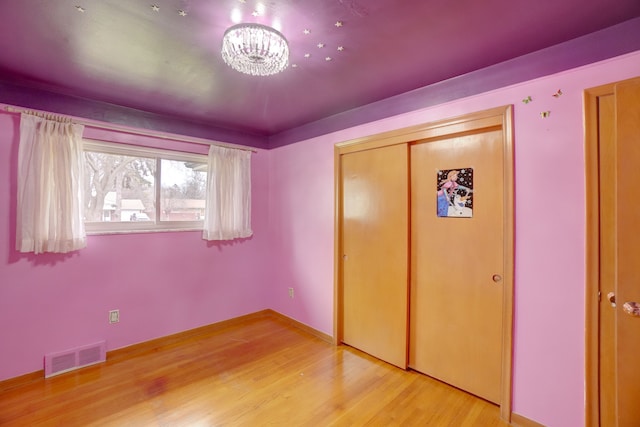 unfurnished bedroom with a closet, light hardwood / wood-style floors, and a notable chandelier