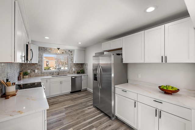 kitchen with sink, light stone countertops, appliances with stainless steel finishes, light hardwood / wood-style floors, and white cabinetry