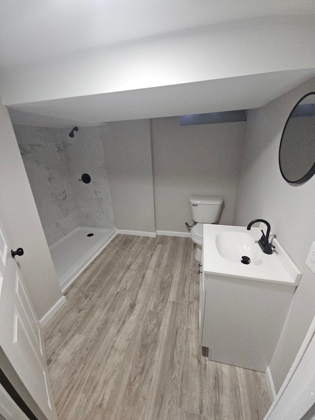 bathroom featuring toilet, vanity, wood-type flooring, and tiled shower