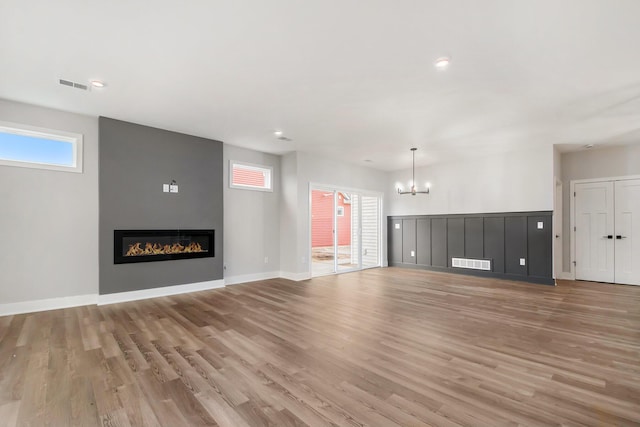 unfurnished living room featuring a fireplace, light wood-type flooring, and a notable chandelier