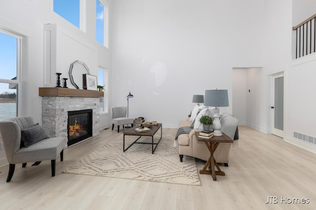 living room featuring light wood finished floors, baseboards, visible vents, and a stone fireplace