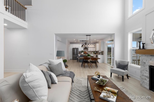 living room featuring a wealth of natural light, a stone fireplace, light wood-type flooring, and a towering ceiling