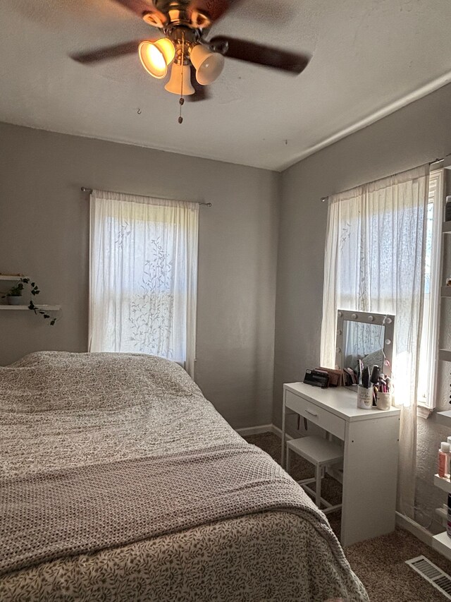 carpeted bedroom featuring baseboards, visible vents, ceiling fan, and multiple windows
