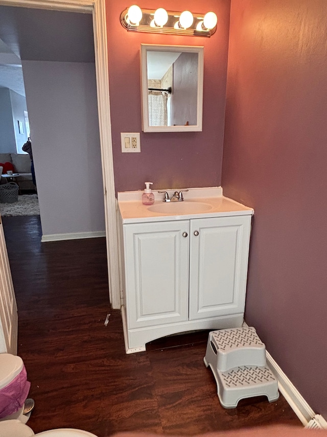 bathroom with toilet, wood finished floors, vanity, and baseboards