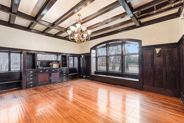 unfurnished living room featuring beam ceiling, light hardwood / wood-style floors, an inviting chandelier, and coffered ceiling