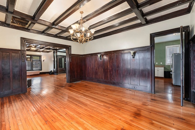 unfurnished dining area with hardwood / wood-style floors, beamed ceiling, coffered ceiling, and a notable chandelier