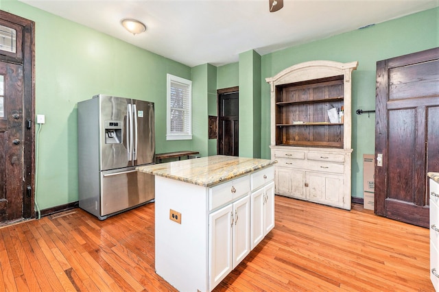 kitchen featuring white cabinetry, a center island, stainless steel fridge with ice dispenser, light stone counters, and light hardwood / wood-style floors