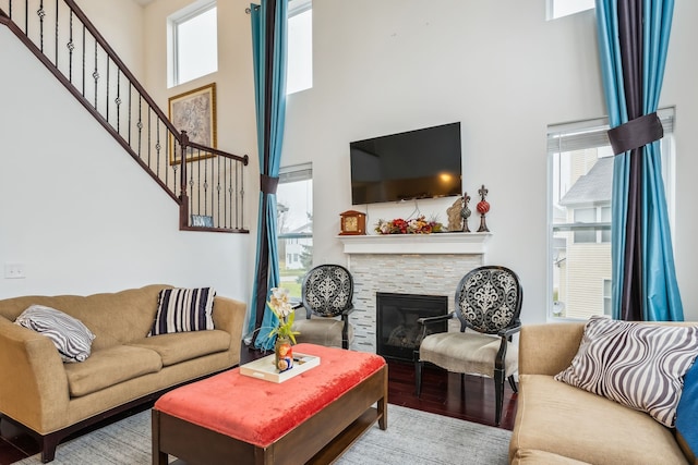 living room featuring a stone fireplace, hardwood / wood-style floors, and a towering ceiling