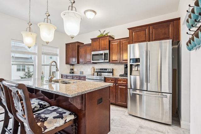 kitchen with a kitchen island with sink, sink, tasteful backsplash, decorative light fixtures, and stainless steel appliances