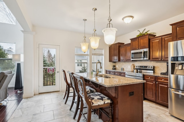 kitchen featuring a center island with sink, sink, hanging light fixtures, a kitchen bar, and stainless steel appliances