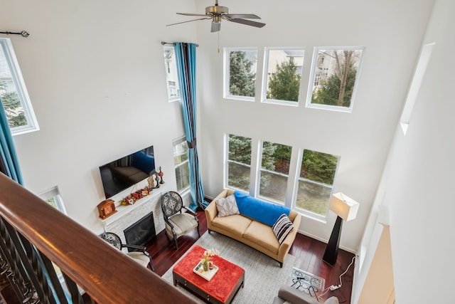 living room featuring ceiling fan, wood-type flooring, a fireplace, and a towering ceiling