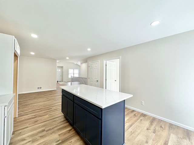 kitchen with white cabinets, a center island, light hardwood / wood-style flooring, and light stone countertops