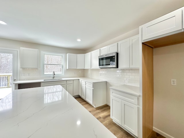 kitchen with light stone countertops, backsplash, a healthy amount of sunlight, sink, and white cabinetry