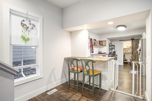 kitchen with wooden counters, a kitchen breakfast bar, dark hardwood / wood-style flooring, sink, and a barn door