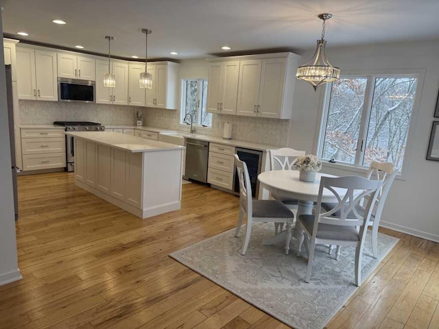 kitchen featuring white cabinetry, a center island, hanging light fixtures, appliances with stainless steel finishes, and light wood-type flooring