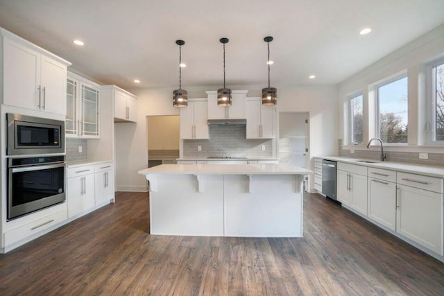 kitchen with a sink, a kitchen island, dark wood-style floors, appliances with stainless steel finishes, and white cabinets