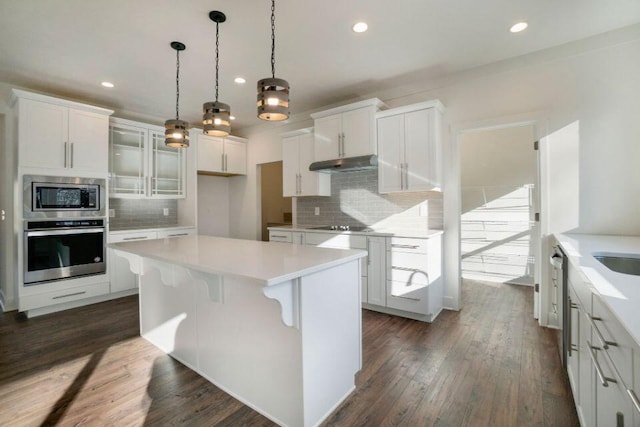 kitchen with a center island, under cabinet range hood, appliances with stainless steel finishes, dark wood-style floors, and white cabinetry