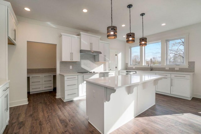 kitchen featuring under cabinet range hood, dark wood-type flooring, a center island, and light countertops