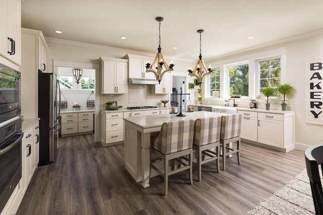 kitchen featuring tasteful backsplash, crown molding, light countertops, an island with sink, and stainless steel appliances