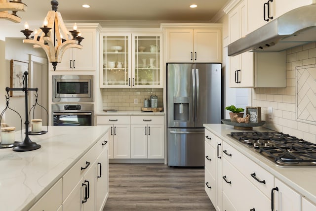 kitchen featuring backsplash, glass insert cabinets, under cabinet range hood, appliances with stainless steel finishes, and dark wood-style floors