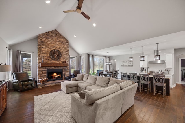 living room featuring ceiling fan, a stone fireplace, dark hardwood / wood-style floors, and high vaulted ceiling