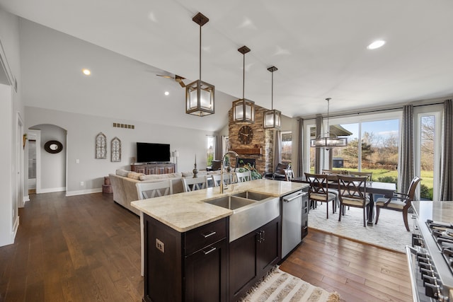 kitchen featuring hanging light fixtures, appliances with stainless steel finishes, light stone countertops, dark hardwood / wood-style floors, and a center island with sink