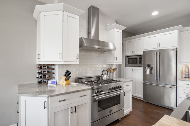 kitchen with premium appliances, backsplash, white cabinets, light stone counters, and wall chimney range hood