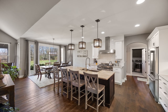 kitchen featuring white cabinets, wall chimney range hood, hanging light fixtures, a center island with sink, and high quality appliances