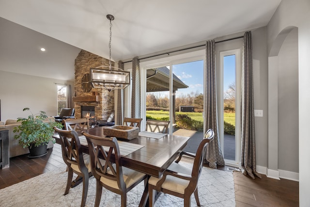 dining space with a notable chandelier, a stone fireplace, and dark wood-type flooring