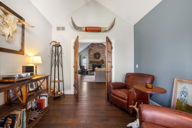 sitting room with dark hardwood / wood-style flooring, lofted ceiling, and a stone fireplace