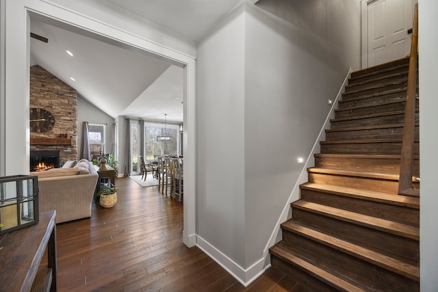 staircase featuring vaulted ceiling, a stone fireplace, and hardwood / wood-style floors